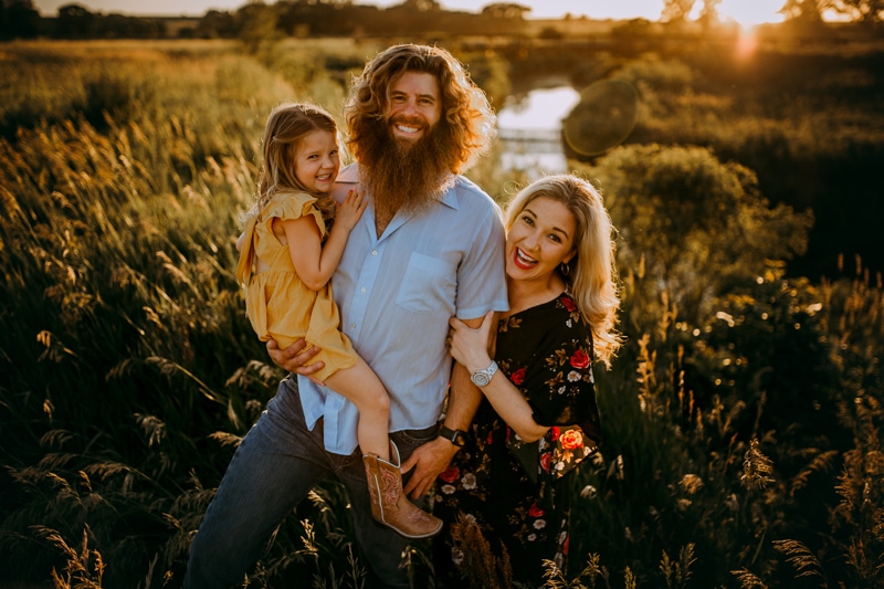 Family Photographer, Husband and wife with their young daughter in a dry grassy field